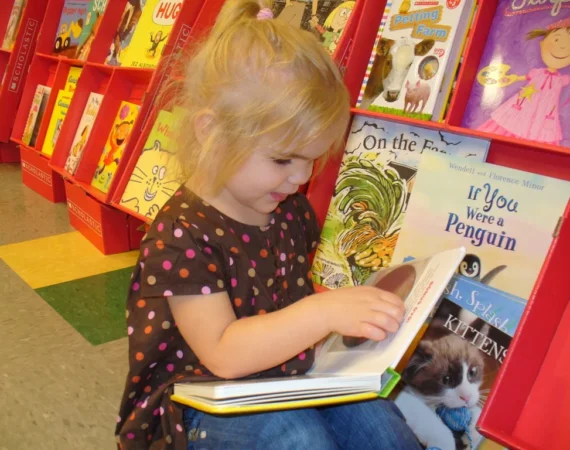 A little girl reading at the Creative Childcare Academy and Camp book fair
